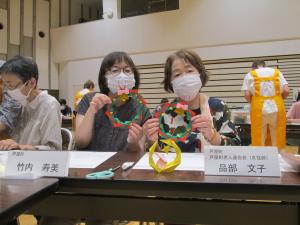 参加者が完成した作品（クリスマスリース）を見せている写真です。